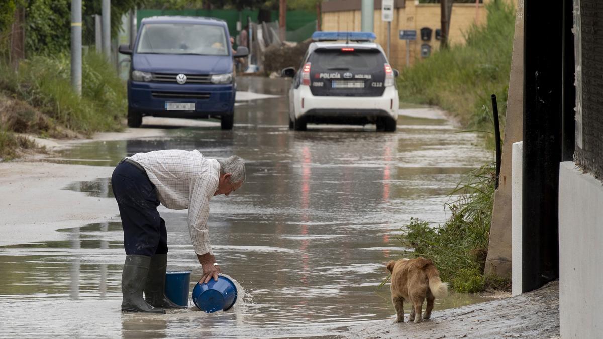 Un hombre retira agua con cubos, en una calle inundada en Molina de Segura, Murcia