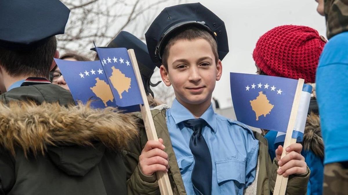 Un joven vestido de agente de policía sostiene una bandera kosovar en una manifestación en Prístina.