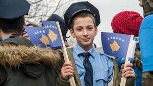 Un joven vestido de agente de policía sostiene una bandera kosovar en una manifestación en Prístina.