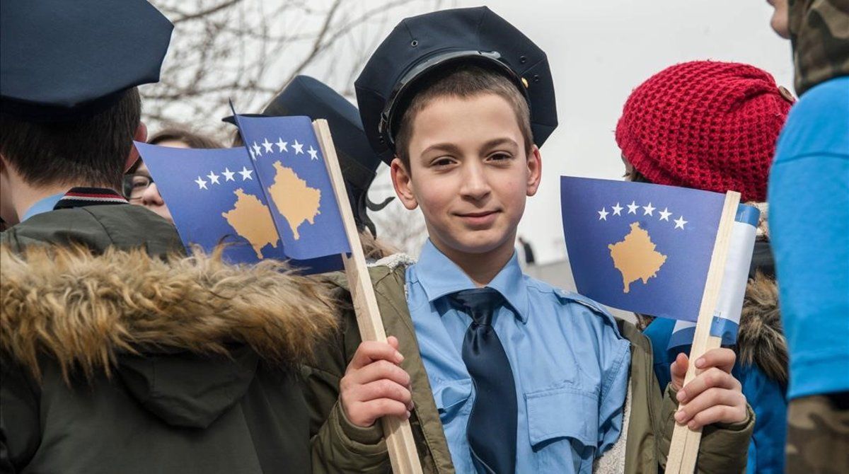 Un joven vestido de agente de policía sostiene una bandera kosovar en una manifestación en Prístina.