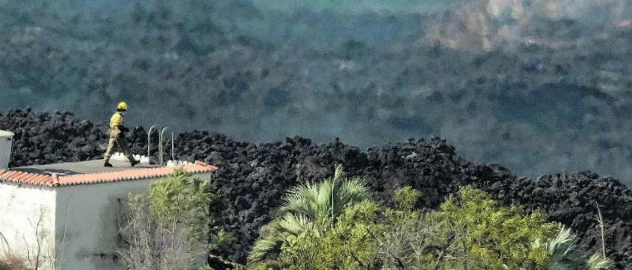 Un bombero sobre una vivienda, junto a la enorme colada del volcán.