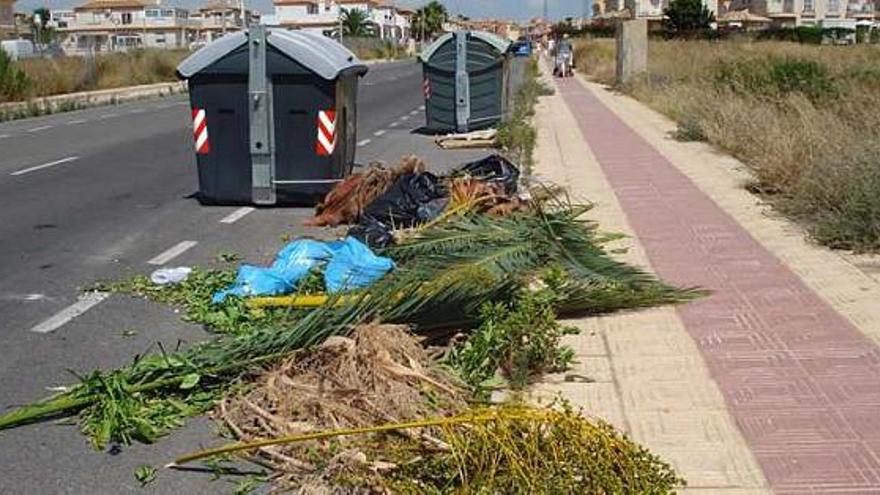 Vista de una calle con malas hierbas y contenedores mal situados.