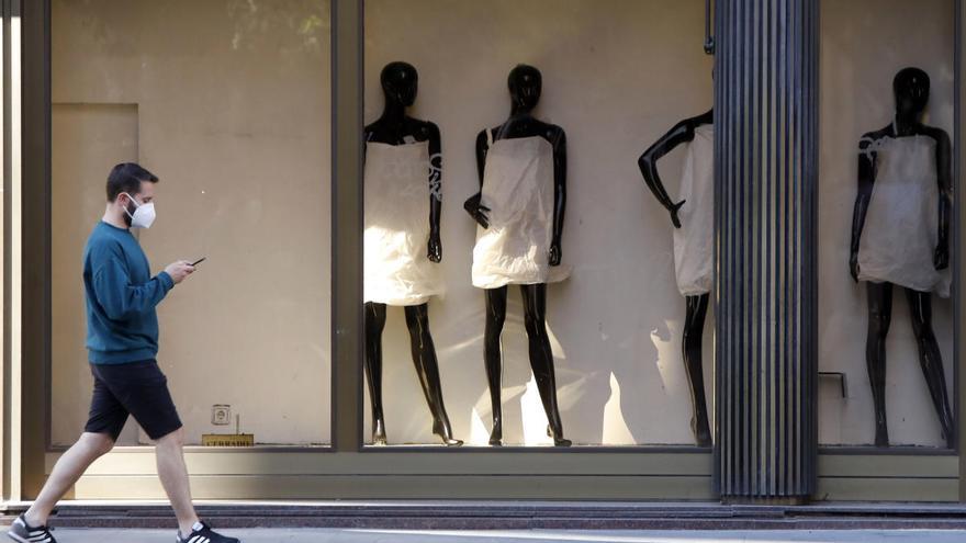 Un hombre con mascarilla pasea por delante de una tienda de ropa