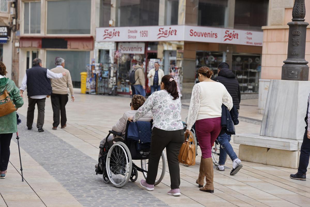 Una cuidadora de una mujer mayor paseando con ella por el centro de Cartagena.