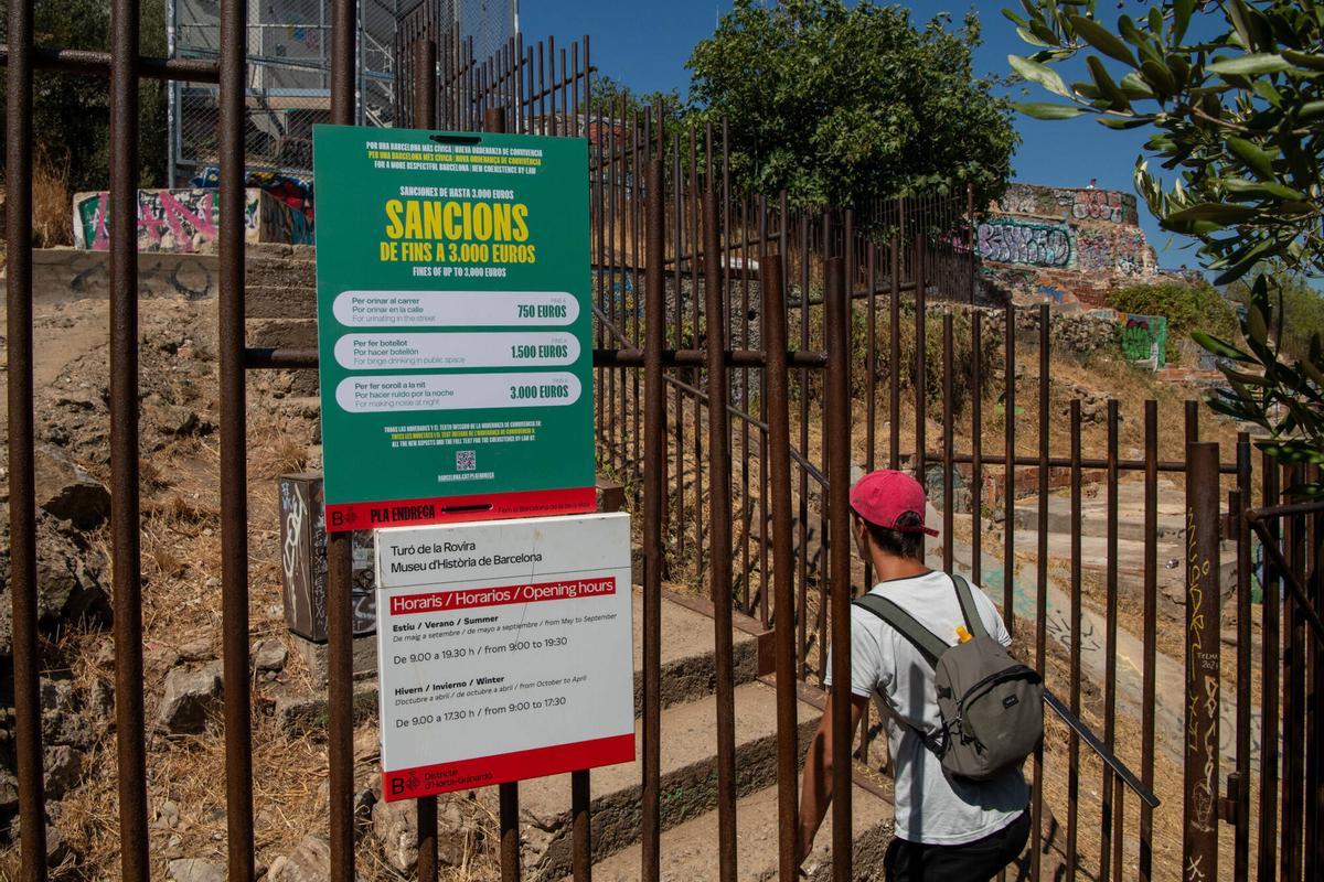 Un turista entrando a los Búnkers del Carmel. En la verja, cartel del ayuntamiento que anuncia sanciones por orinar en la calle, hacer botellón y hacer ruido. Barcelona, 5 de agosto de 2026. Foto: Belén González/ EP