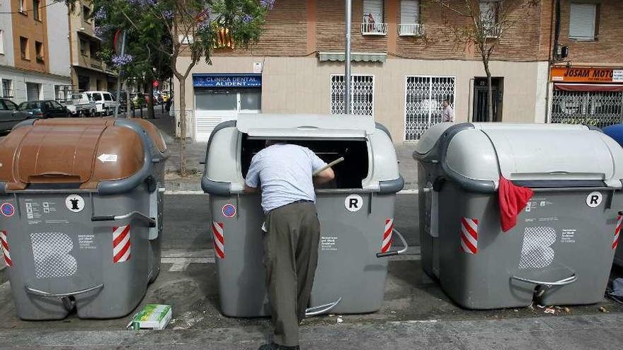 Un hombre rebusca dentro de un contenedor de basura.