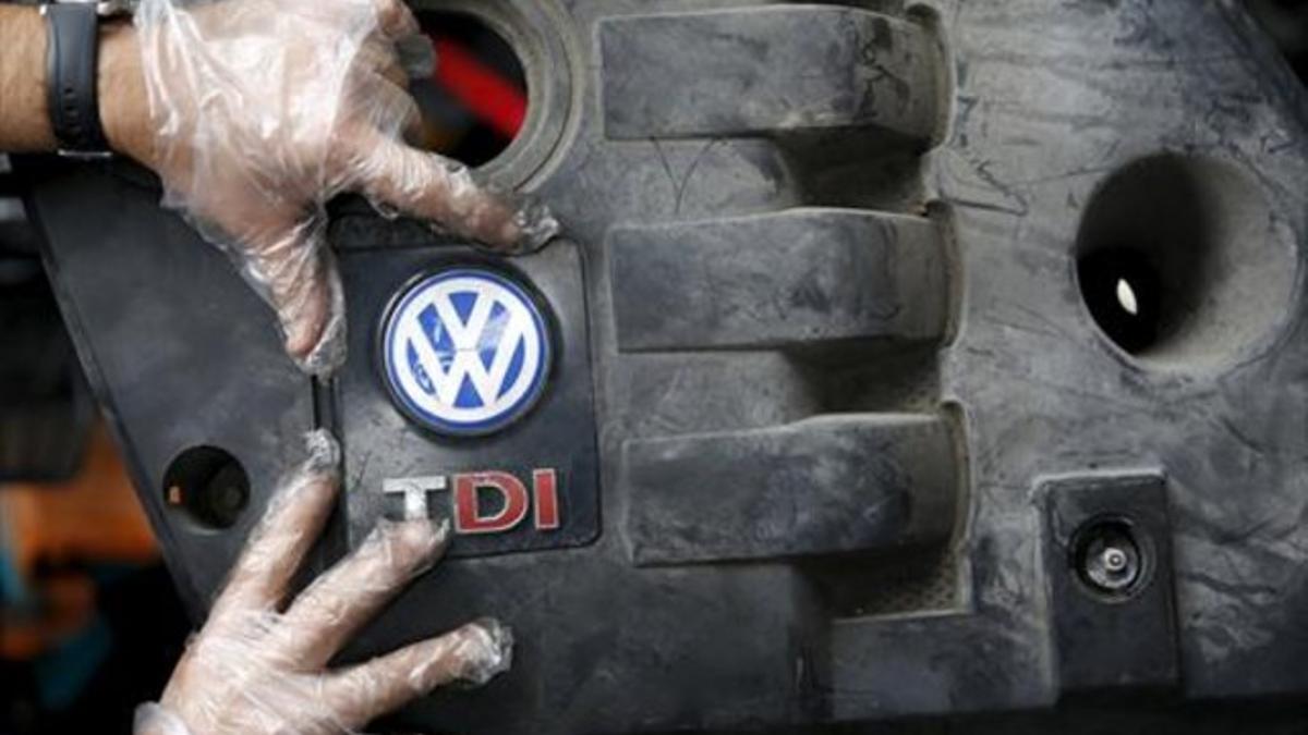 Un trabajador muestra el logo de un motor diésel TDI de Volkswagen de segunda mano en Jelah, Bosnia.