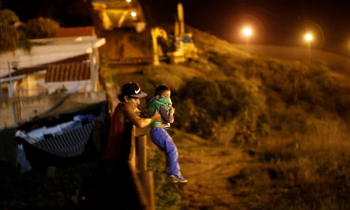 Un migrante hondureño, que forma parte de una caravana de miles de habitantes de América Central que intenta llegar a los Estados Unidos, ayuda a un niño a saltar la valla para cruzarla ilegalmente en Tijuana, México.