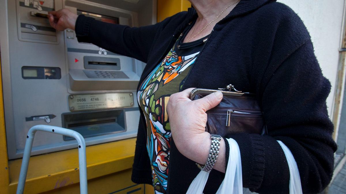 Una mujer saca dinero de un cajero con el monedero agarrado