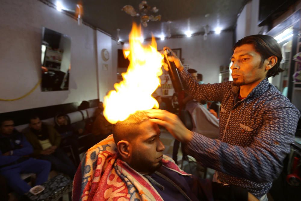 El barbero palestino Ramadan Odwan corta el pelo con fuego a su cliente en una peluquería del sur de la Franja de Gaza.