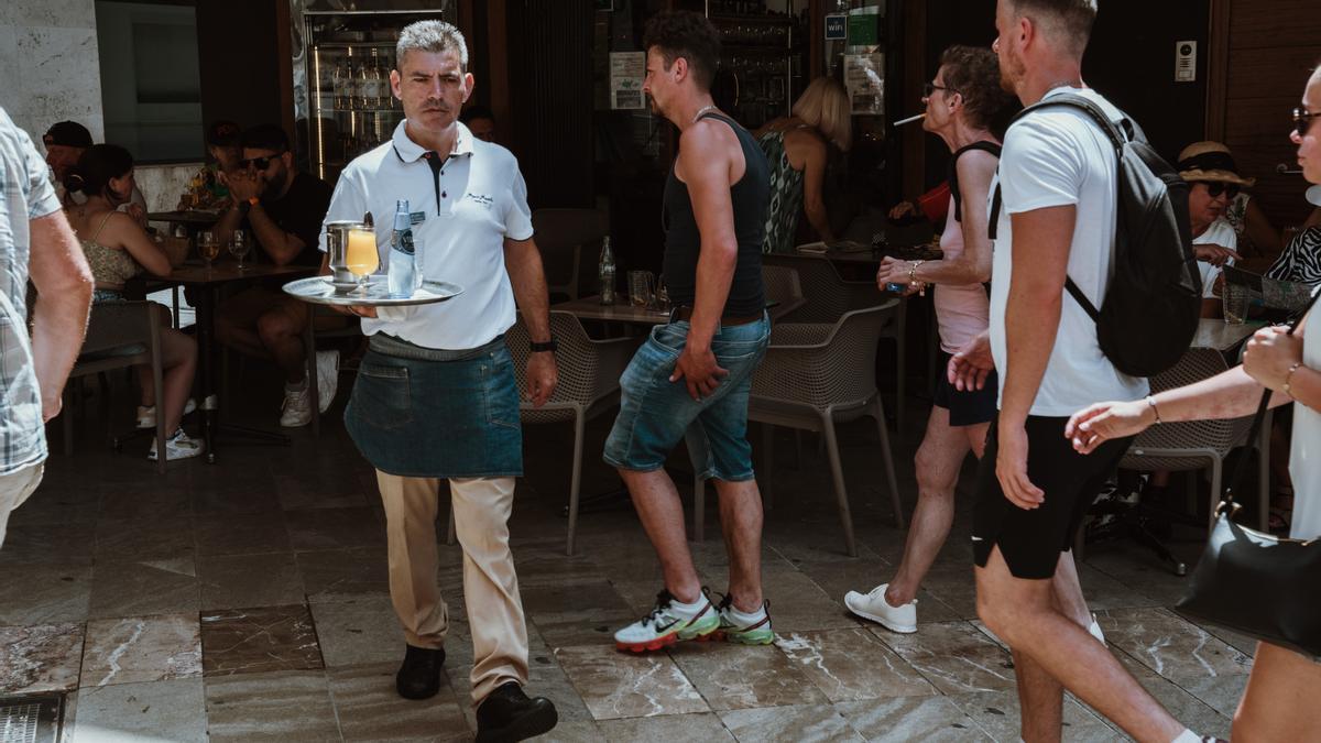 Un trabajador de un bar en el centro de Palma mientras pasean los turistas.