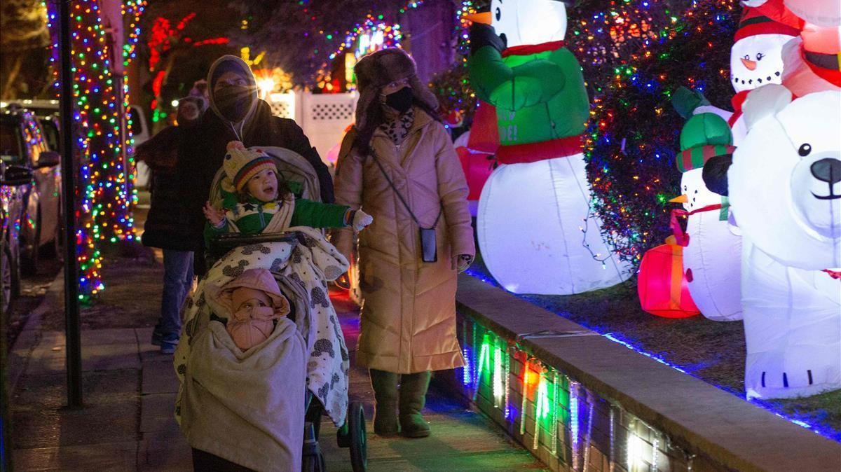 Una familia camina por una calle de Brooklyn, Nueva York, con las casas decoradas con motivos navideños.