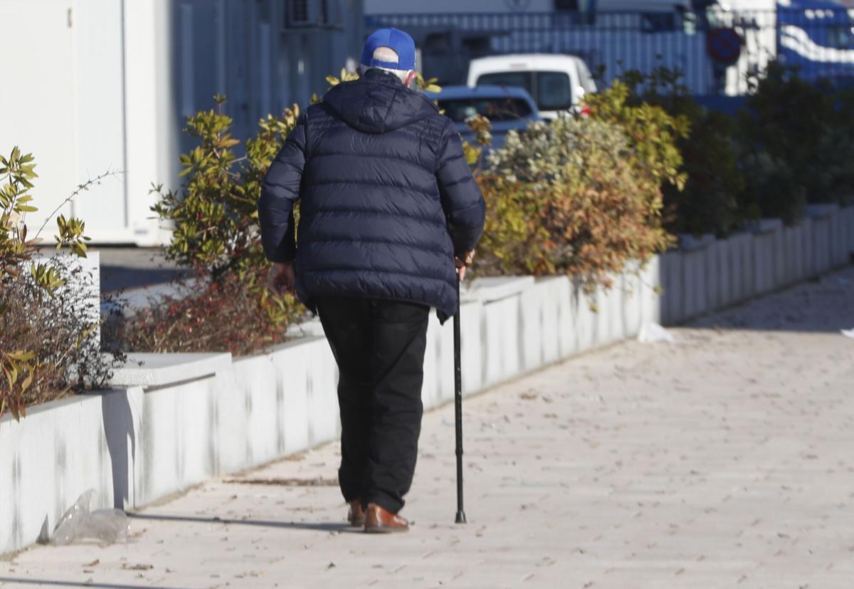 Un señor mayor andando por la calle con un bastón.