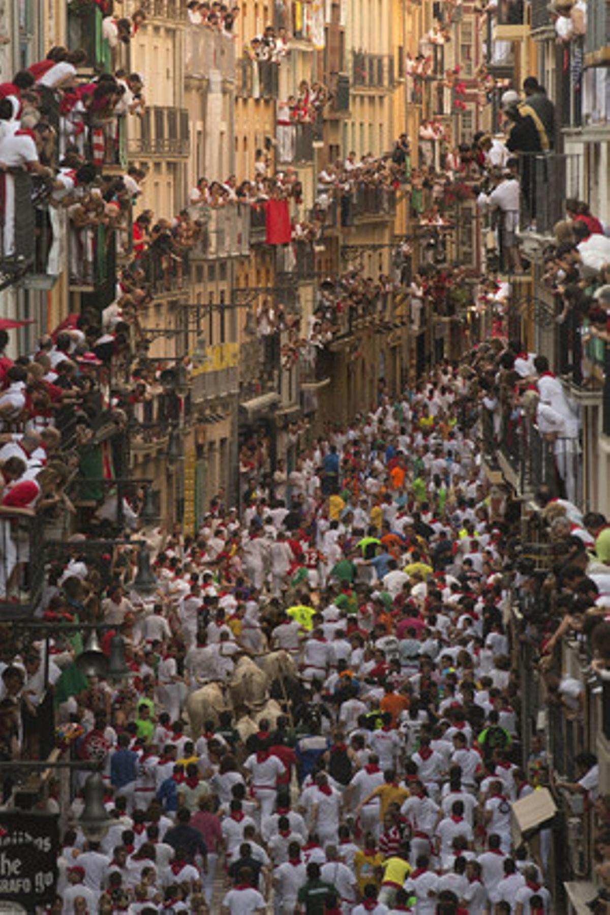 Els corredors pel carrer Estafeta mentre molts espectadors miren des dels balcons.