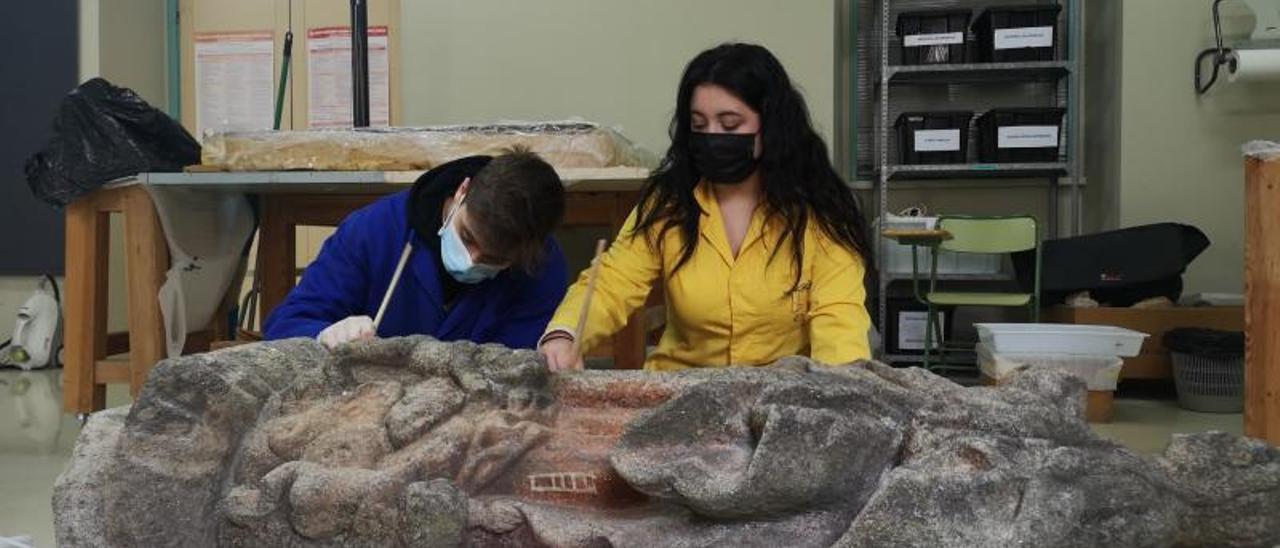 Los alumnos limpian la superficie de la escultura de piedra.