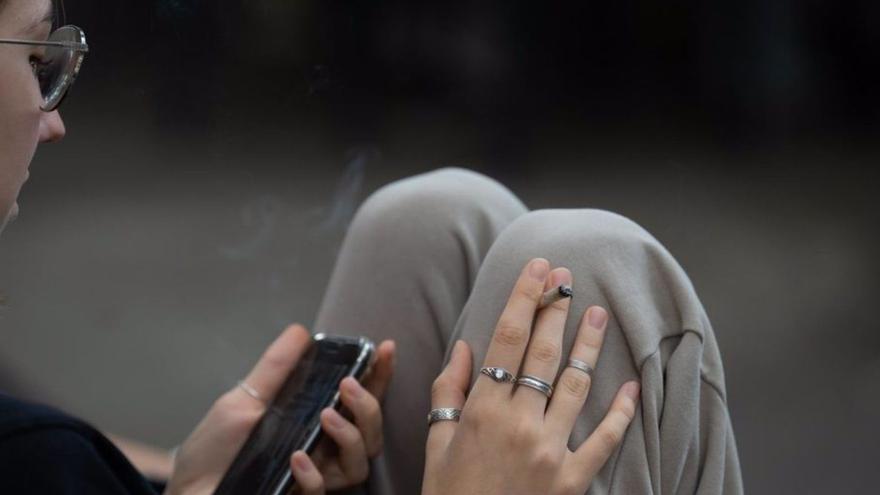 Una joven fuma mientras consulta su 
teléfono móvil.  // Lola Luceño