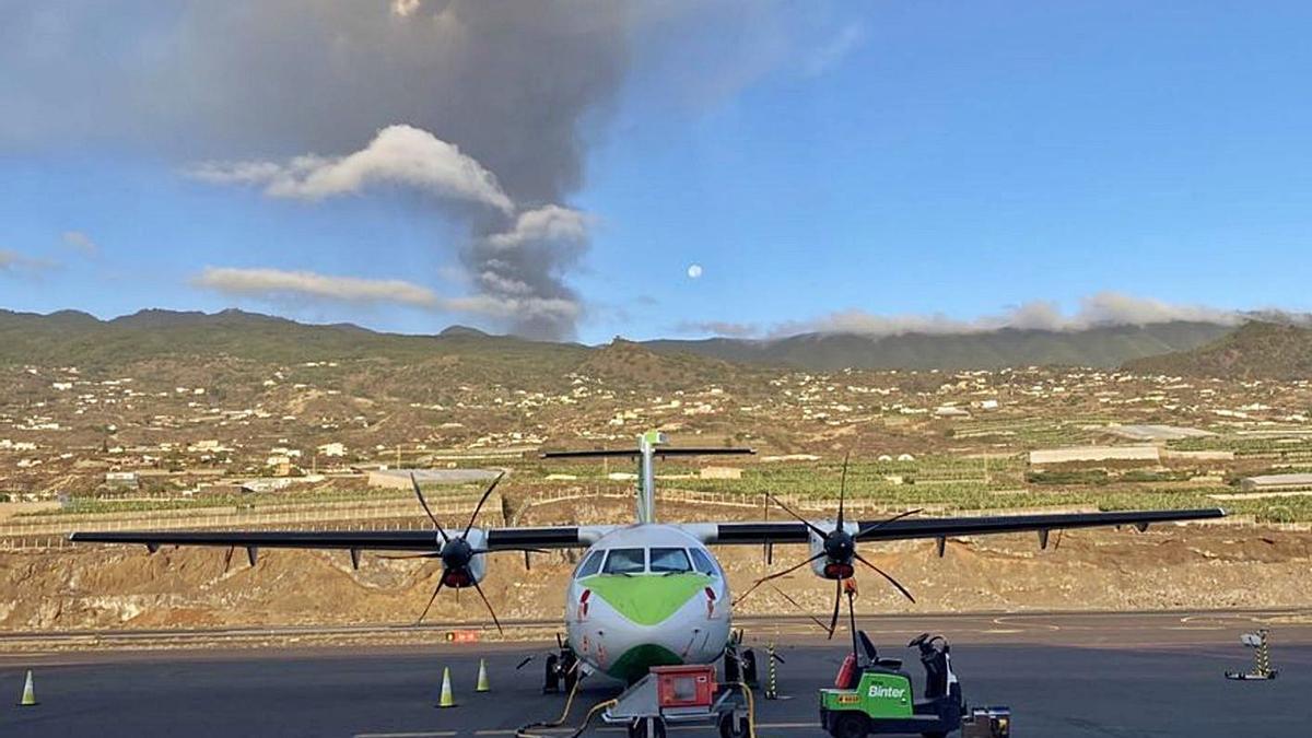 Un avión de Binter en el aeropuerto de Mazo, en La Palma, y detrás la columna de humo del volcán.