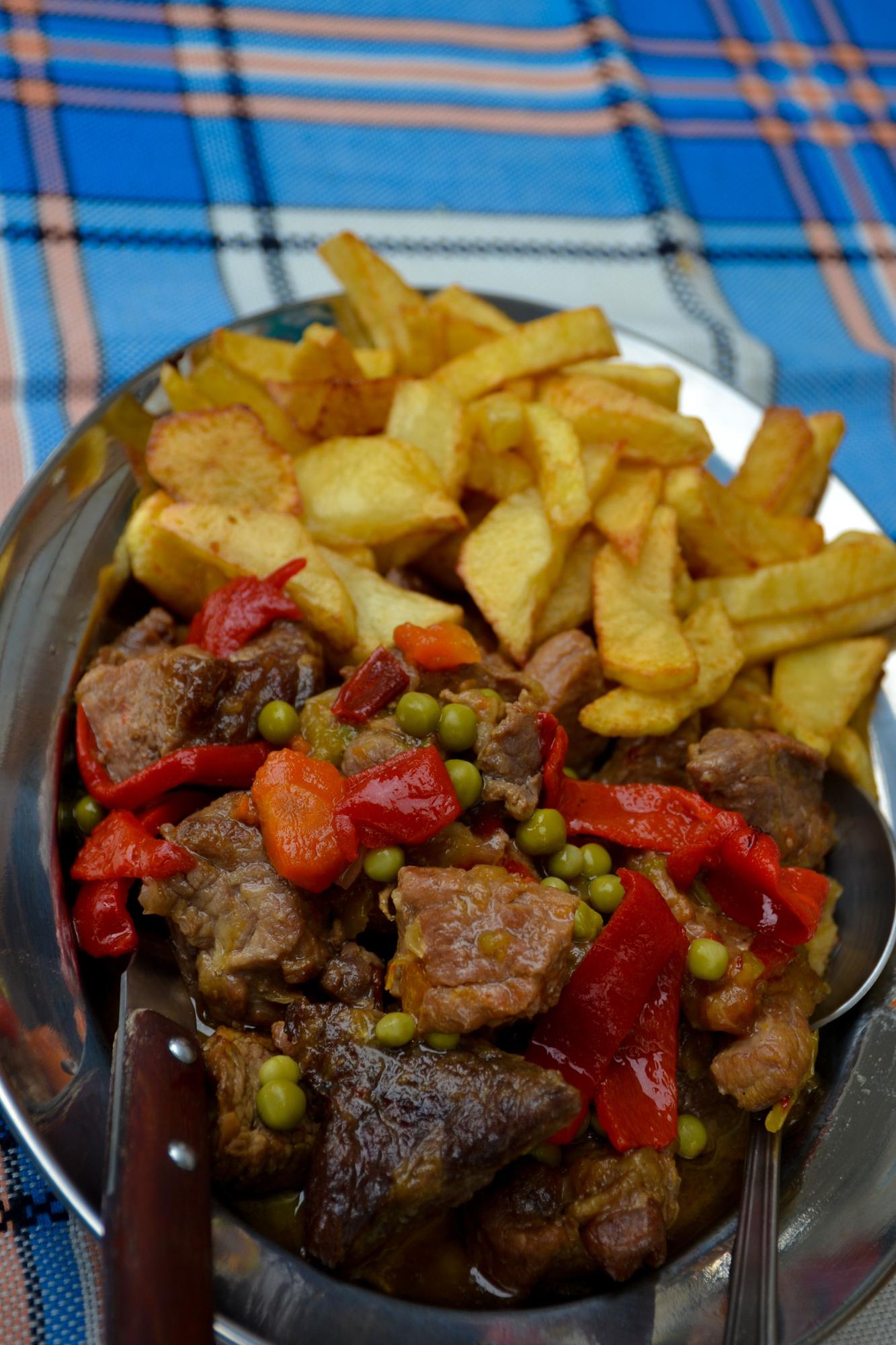 Carne guisada al modo tradicional acompañada de pimientos, guisantes y patatas fritas.