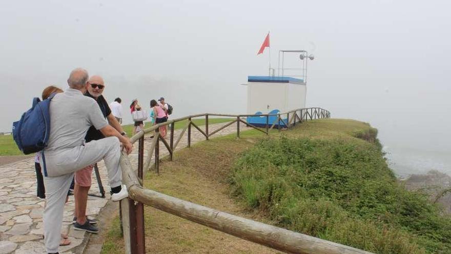 Turistas en la playa, cubierta por la niebla, ayer a mediodía, con la bandera roja ondeando.