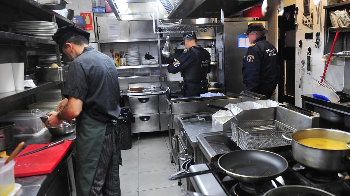 Dos agentes de la Unidad de Establecimientos y Actividades (UEAC) de la Policía Local de Elche revisan a fondo la cocina de un loca