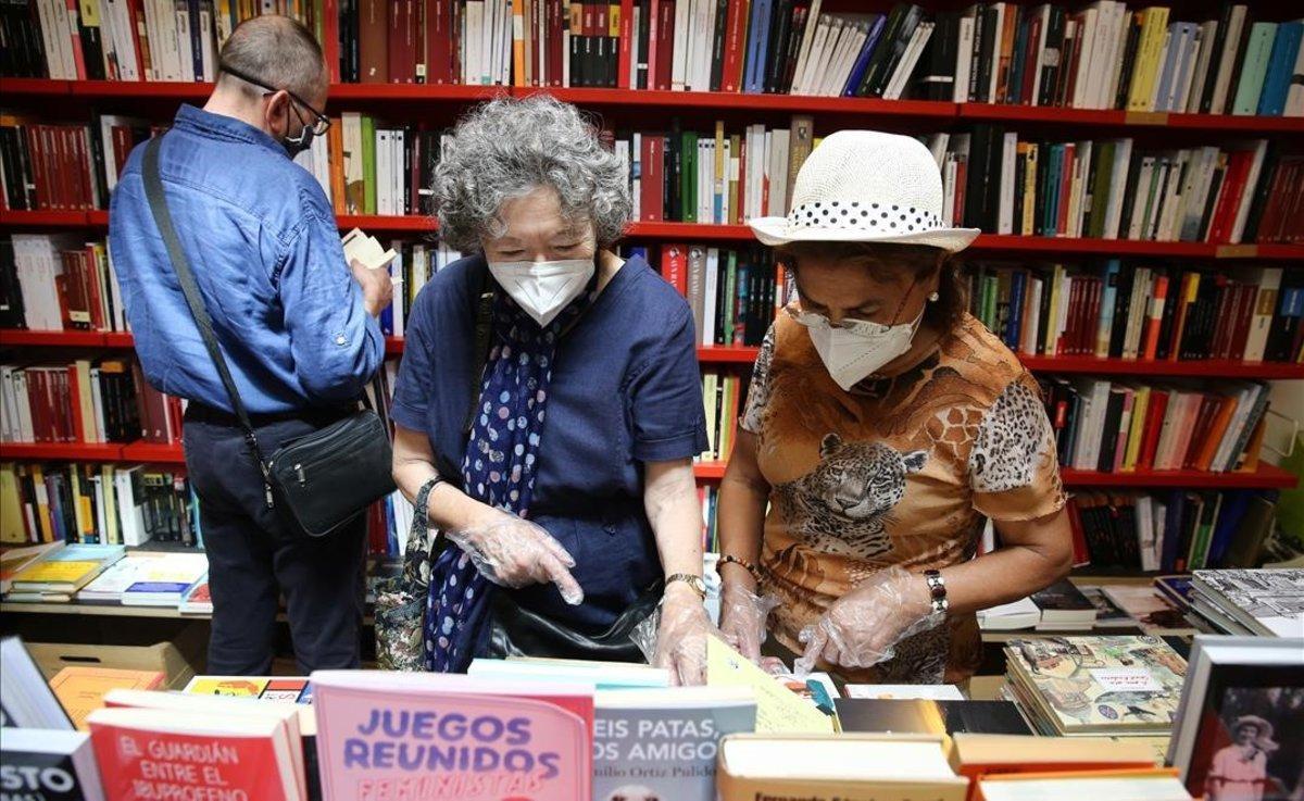 Dos mujeres con guantes miran ejemplares en la librería Documenta de Barcelona.