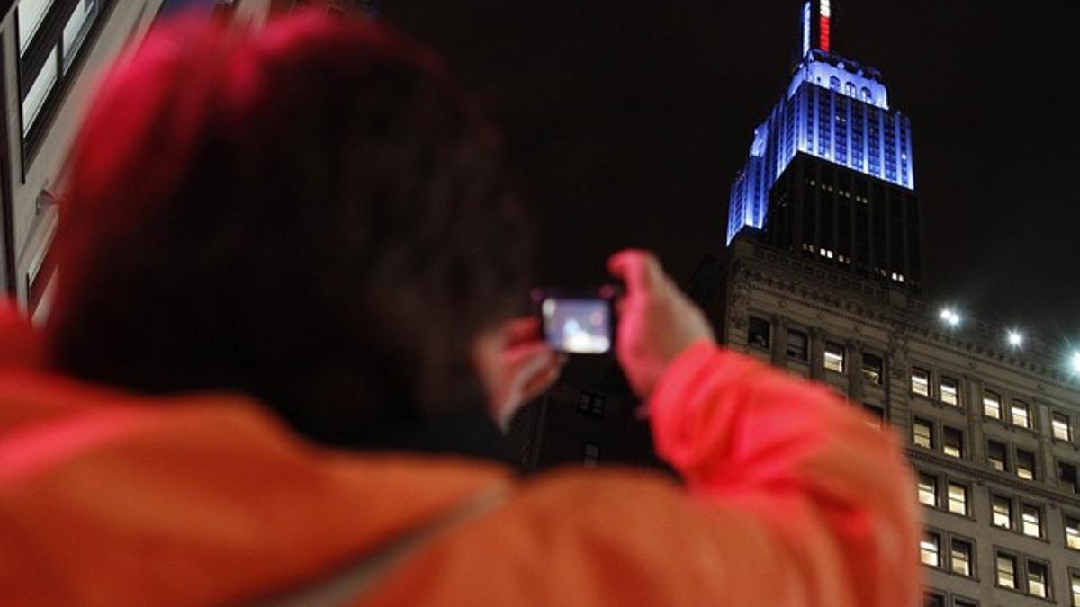 Una mujer toma una foto del Empire State, iluminado de azul, en honor a Obama, ganador de las elecciones.