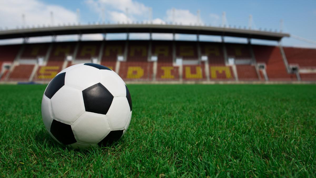 Balón de fútbol sobre césped con fondo de estadio