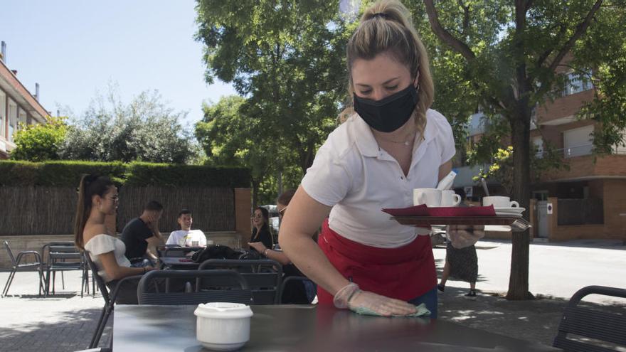 Laura Corominas neteja i desinfecta una taula després que uns clients l&#039;hagin deixat lliure i abans no s&#039;hi asseguessin uns altres