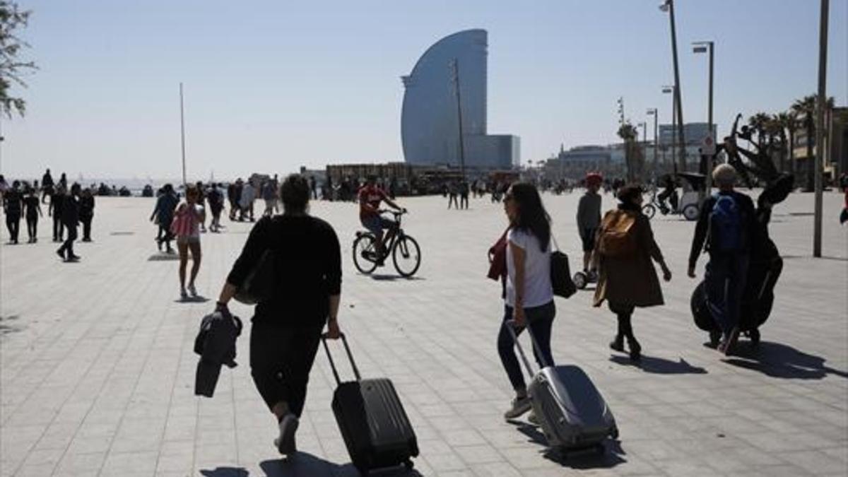 Turistas portan sus equipajes en el barrio de la Barceloneta.