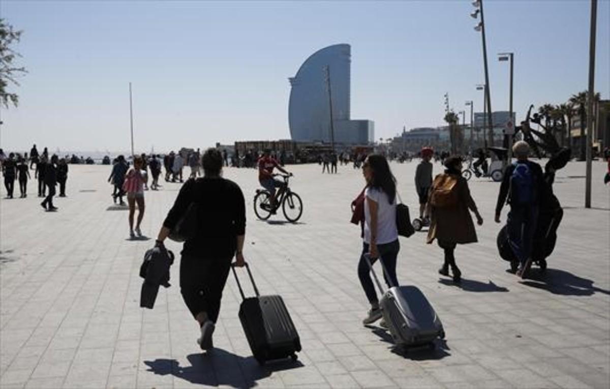 Turistas portan sus equipajes en el barrio de la Barceloneta.