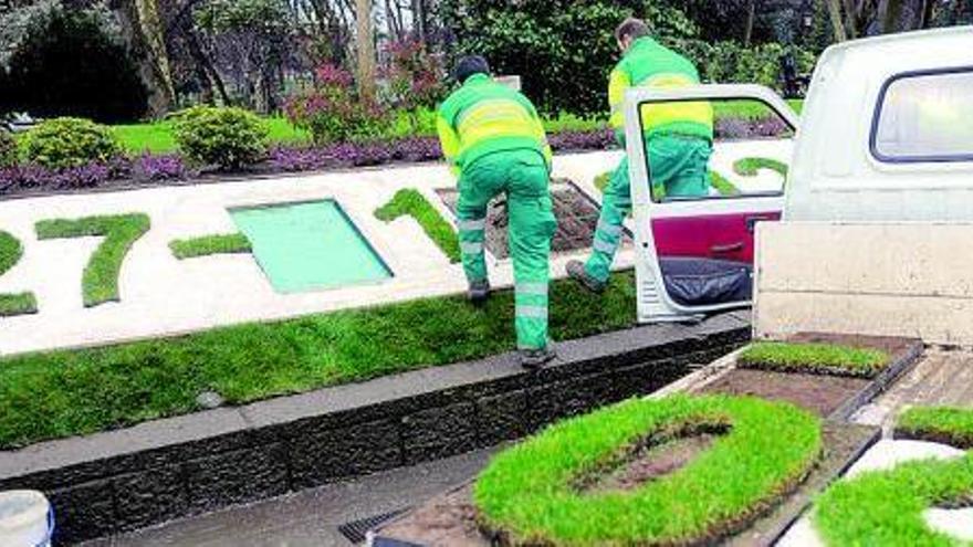 Dos operarios del Servicio de Parques y Jardines reparan los desperfectos del parterre con la fecha.