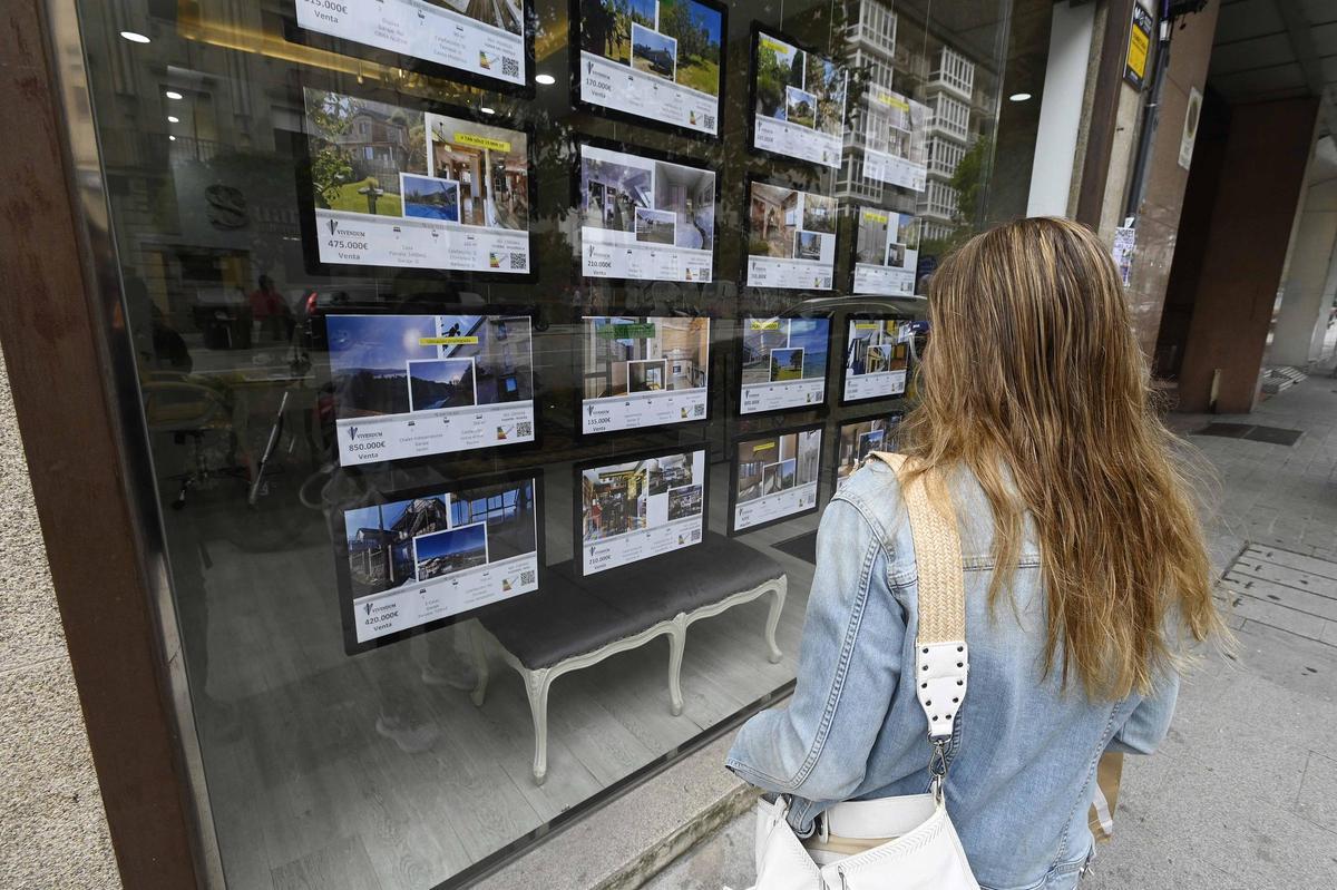 Una mujer mirando el escaparate de una inmobiliaria de Vigo con anuncios de alquiler y venta de inmuebles.