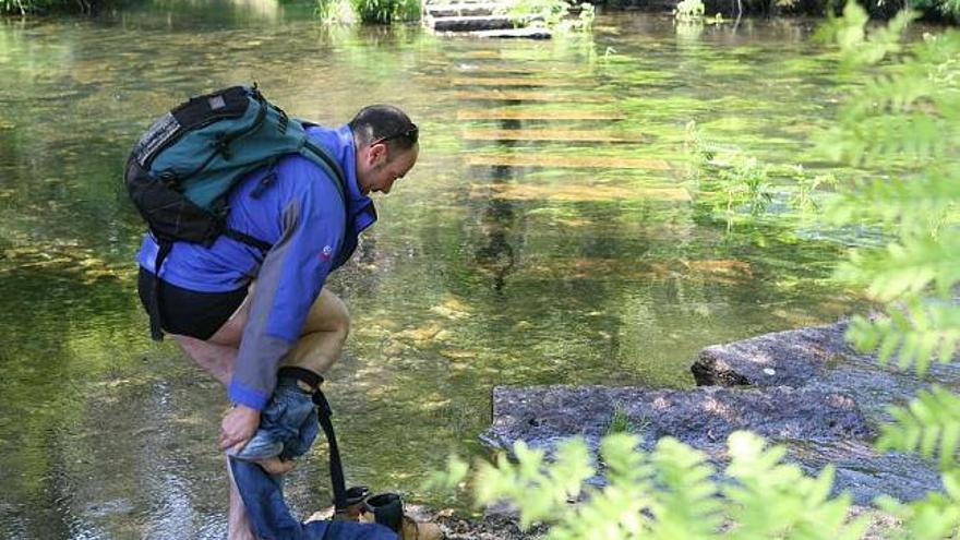 Un peregrino que realiza la ruta de Fisterra a Muxía se quita la ropa para poder cruzar el río Castro. / l. o.