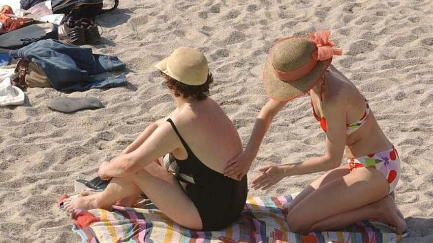 Una mujer pone crema fotoprotectora a otra en la playa de Riazor. / víctor echave
