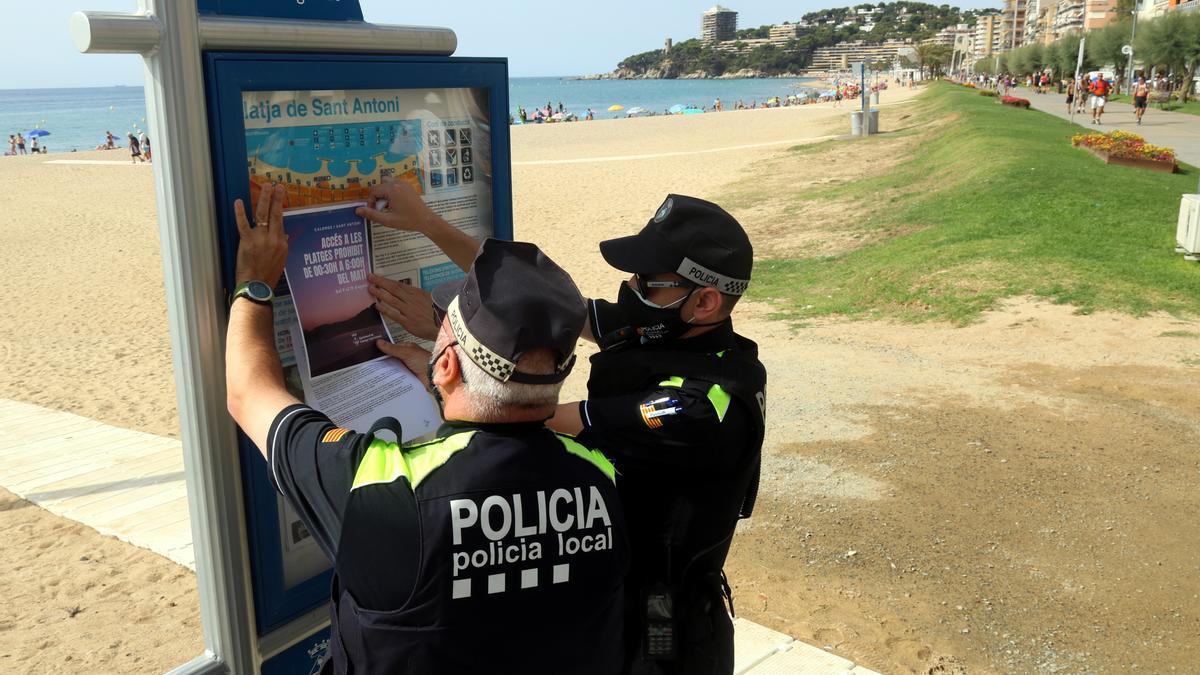 Dos agents de la Policia Local de Calonge i Sant Antoni enganxant el cartell que prohibeix l&#039;accés a les platges de matinada