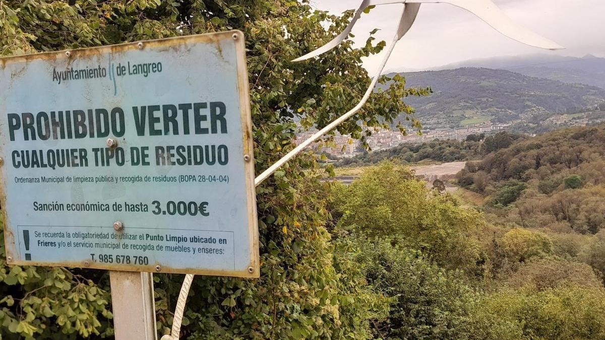 Cartel que avisa de la prohibición de tirar basura en Cuturrasu, con la escombrera de Ibedrola detrás y Langreo al fondo.