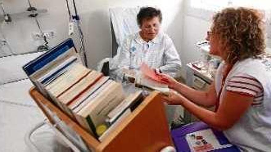 La voluntària de l&#039;Associació Biblioarreu mostra l&#039;oferta de llibres a una pacient.