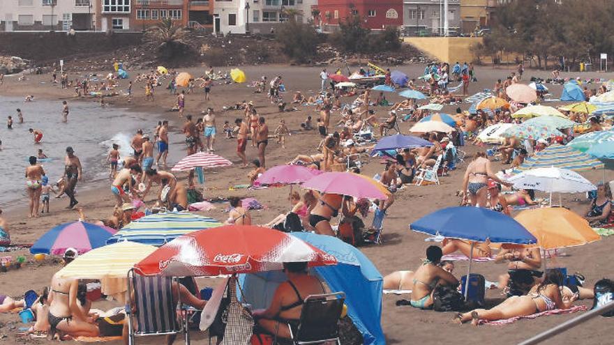 Bañistas en la playa de Melenara, al fondo, viviendas en Clavellinas.