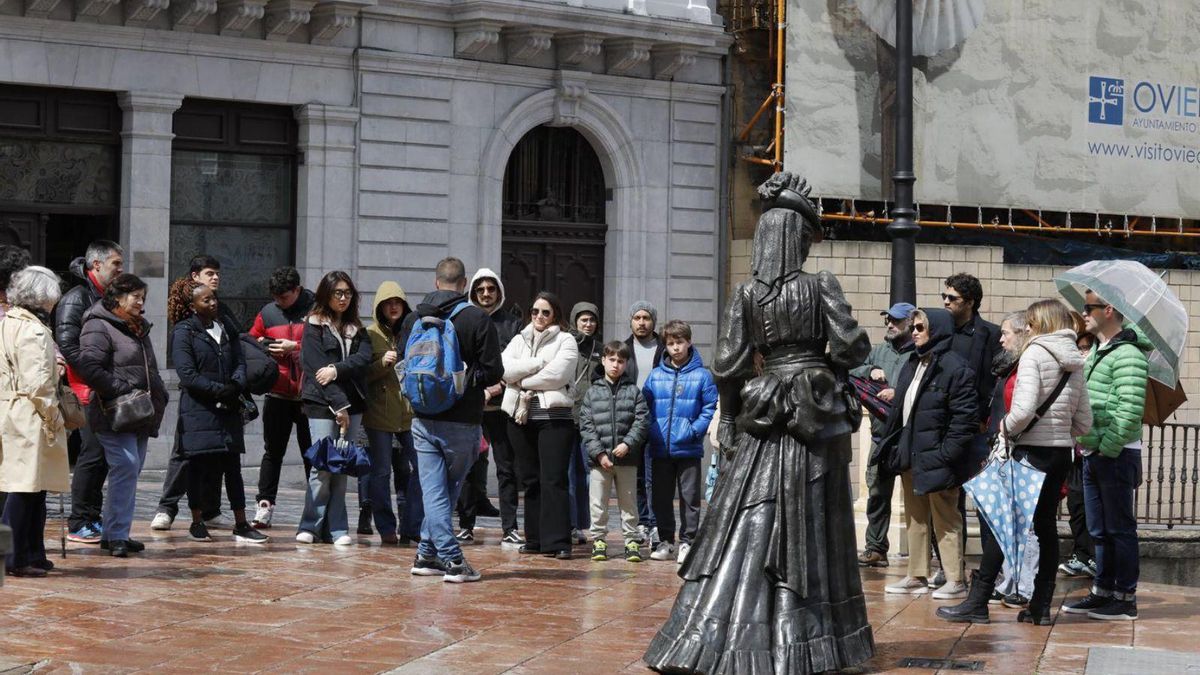Turistas, con abrigos y paraguas, de visita guiada por Oviedo ayer. | FERNANDO RODRÍGUEZ