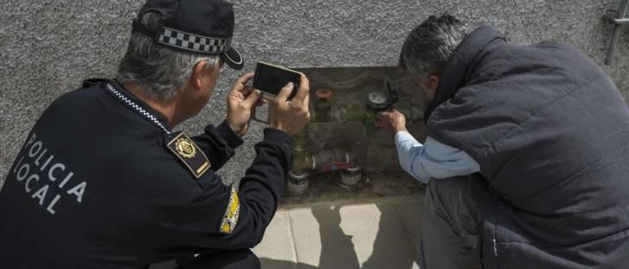 Un agente de la Policía Local de Elche examina con un técnico un contador para detectar posibles irregularidades, en una instalación de la ciudad.