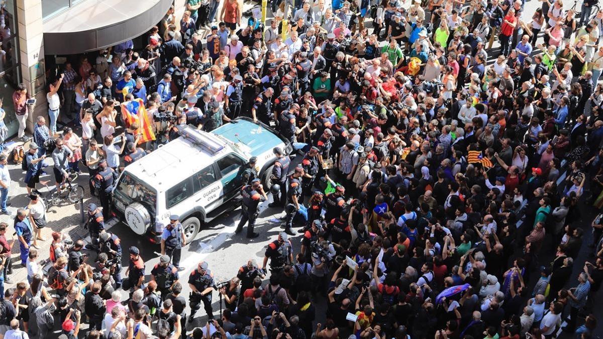 Decenas de personas intentan impedir que salga el coche de la Guardia Civil tras el registro al Departament d'Afers Exteriors de la Generalitat.