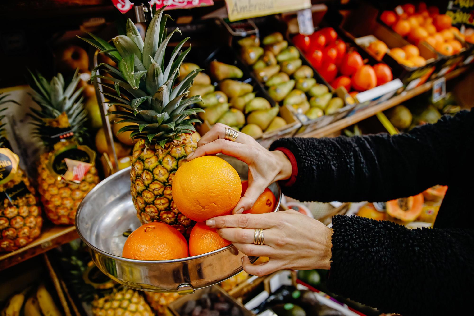 Archivo - Una persona pesa naranjas y una piña en una frutería