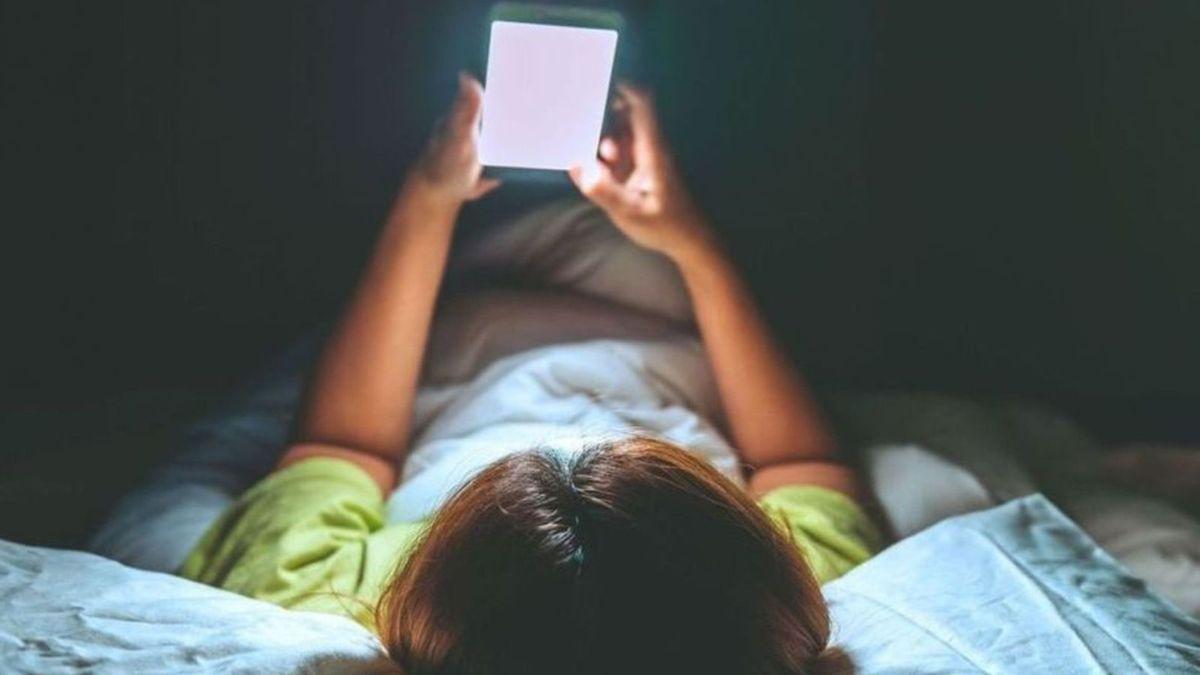 Un niño mirando la pantalla de un móvil en su cama.