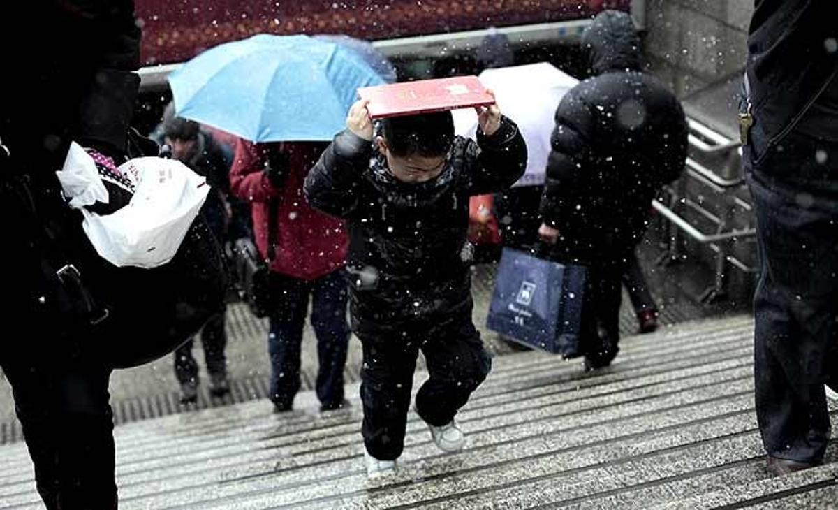 Un nen es tapa el cap amb una carpeta perquè no es mulli a causa de la neu a Xangai (Xina).