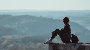 Una joven sentada en una colina mirando al horizonte.
