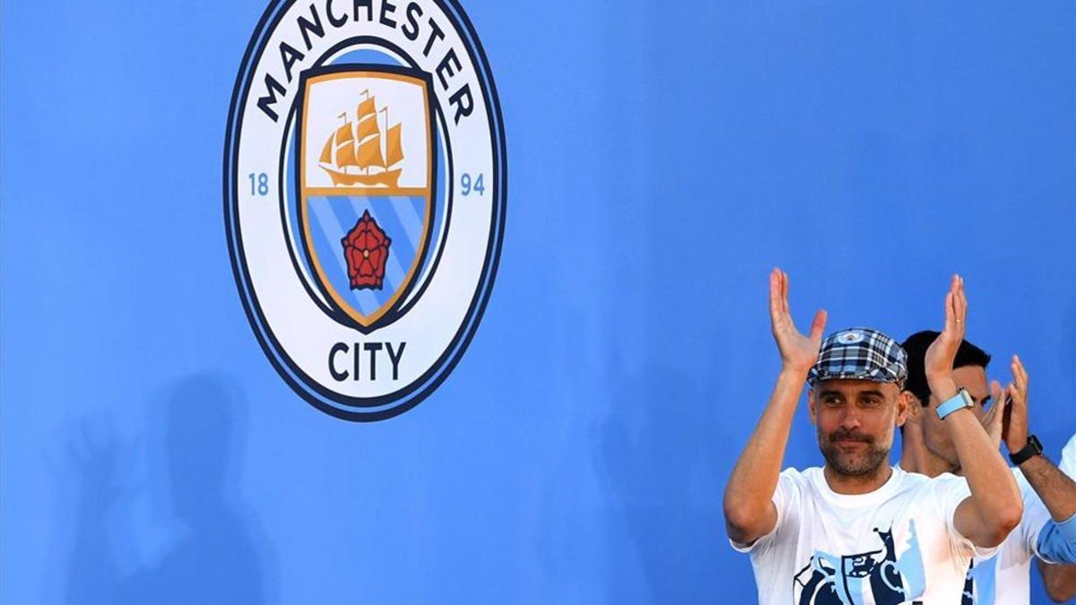 Pep Guardiola junto al escudo del City