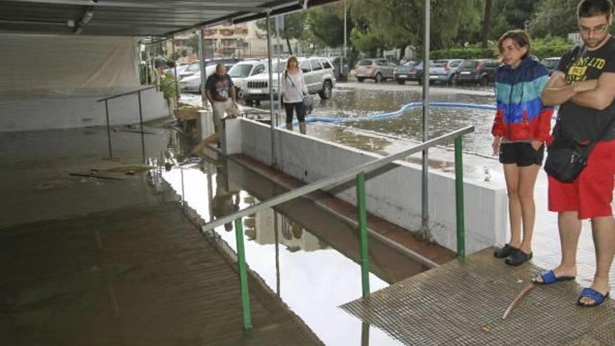 Varias personas observan un local comercial y una calle inundada en la playa de Gandia durante uno de los habituales episodios de fuertes lluvias.