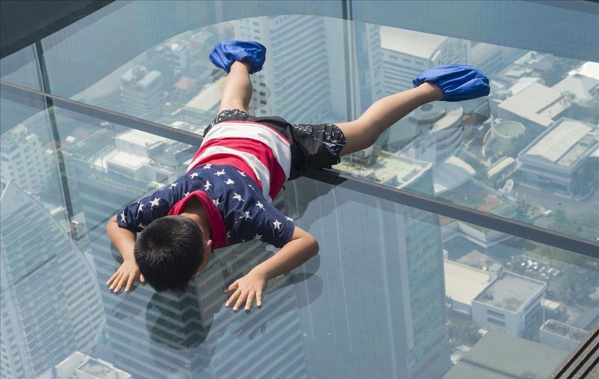 Un niño mira desde la pasarela de vidrio en el piso 78 del rascacielos King Power Mahanakhon, la plataforma de observación más alta de Bangkok durante un día contaminado en la ciudad.