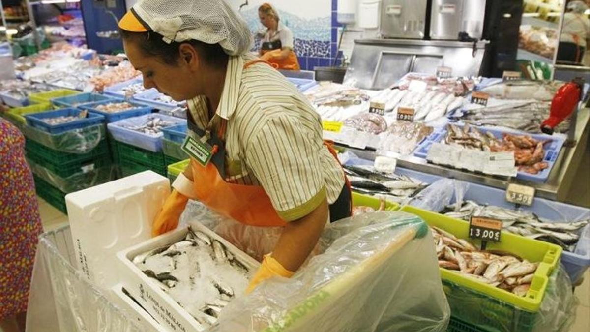 Una joven prepara el mostrador de la pescadería de un supermercado.