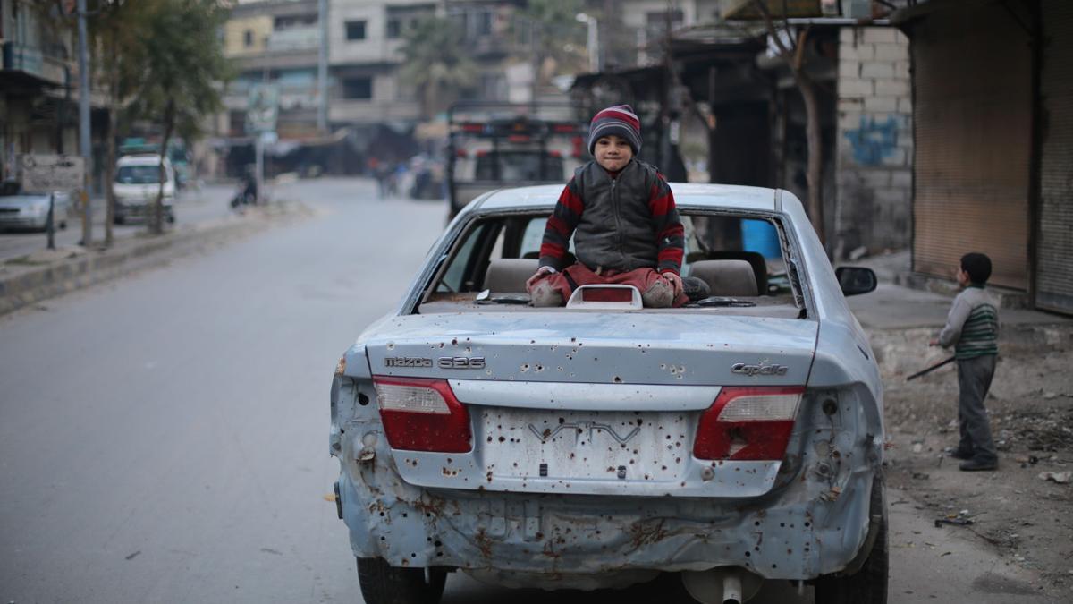 Un niño sirio sentado sobre un coche dañado por las explosiones del este de Ghouta.